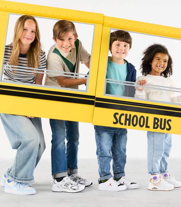 Four happy kids are wearing white sneakers and posing with school bus photo frame