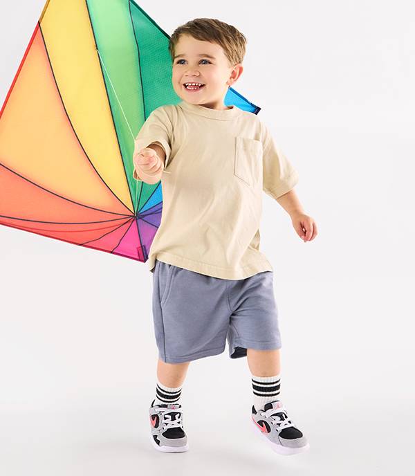 A young happy boy is wearing sneakers and flying a kite