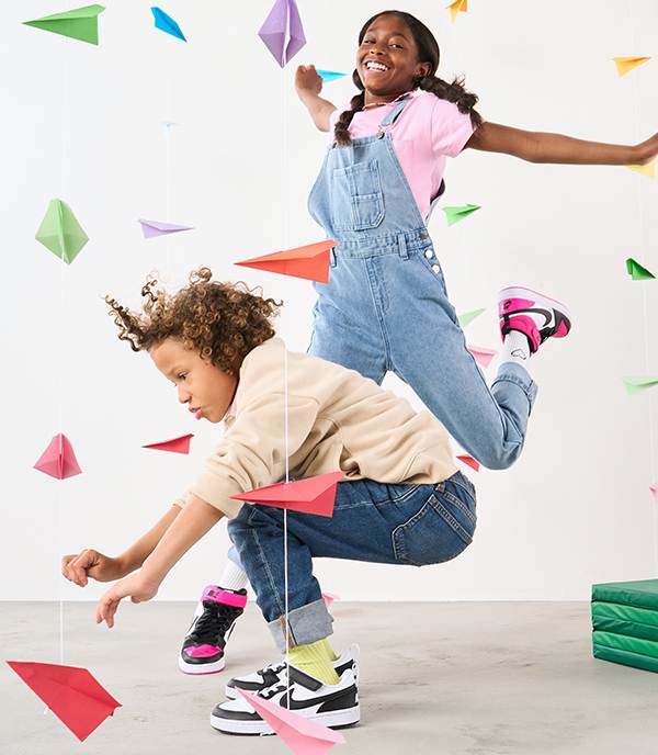Two happy kids wearing Nike Sneakers are having fun times with paper planes around them