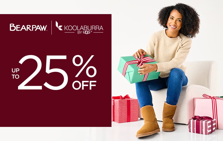 A young woman smiling at the camera sitting in a chair holding a present while wearing cozy Koolaburra by Ugg slippers.		