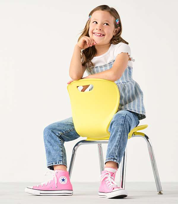 A happy girl sitting on children's chair wearing pink cute Converse sneakers