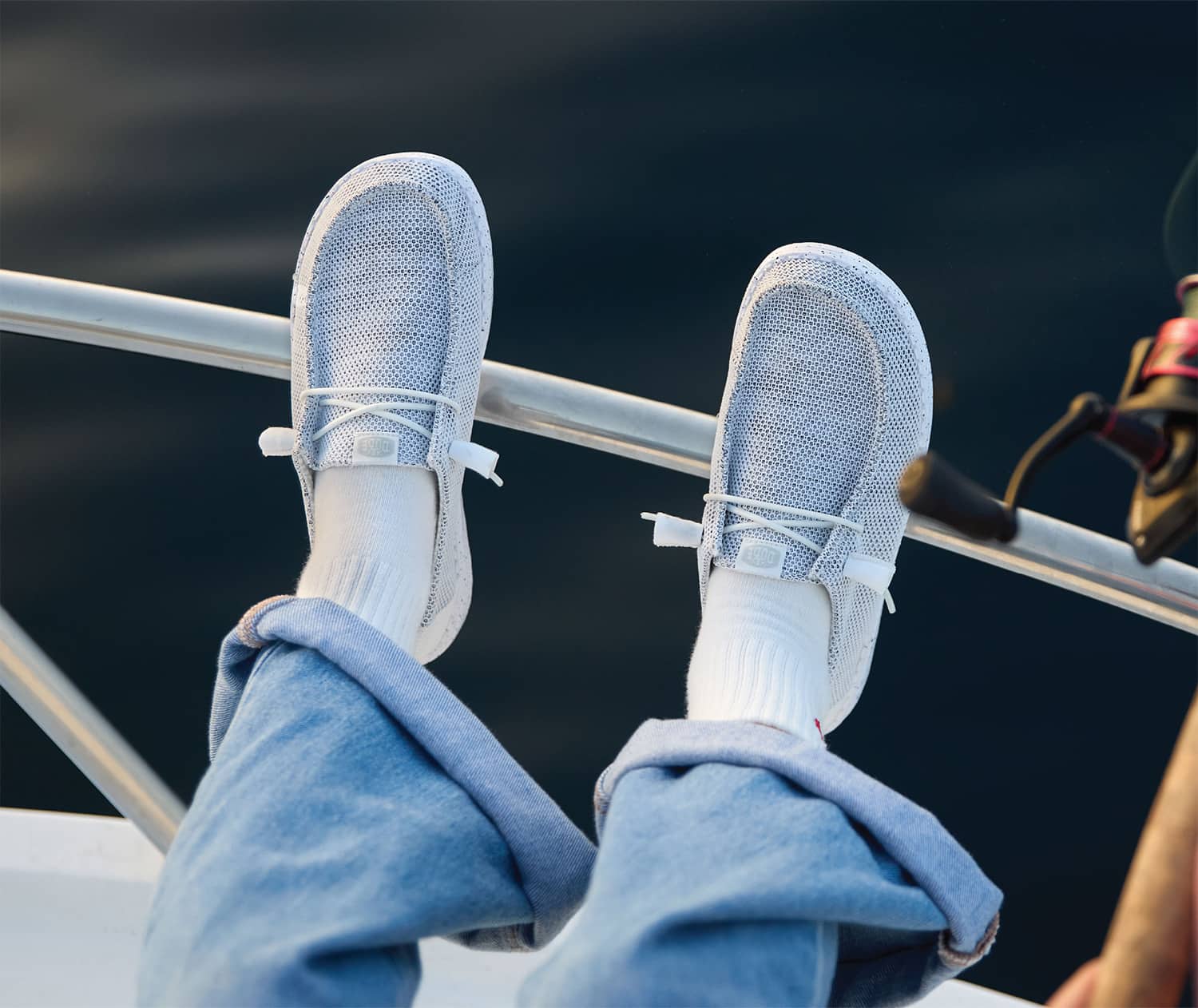 A closeup lifestyle image of brown furry women's HEYDUDE wendy slippers being worn outside on a deck.