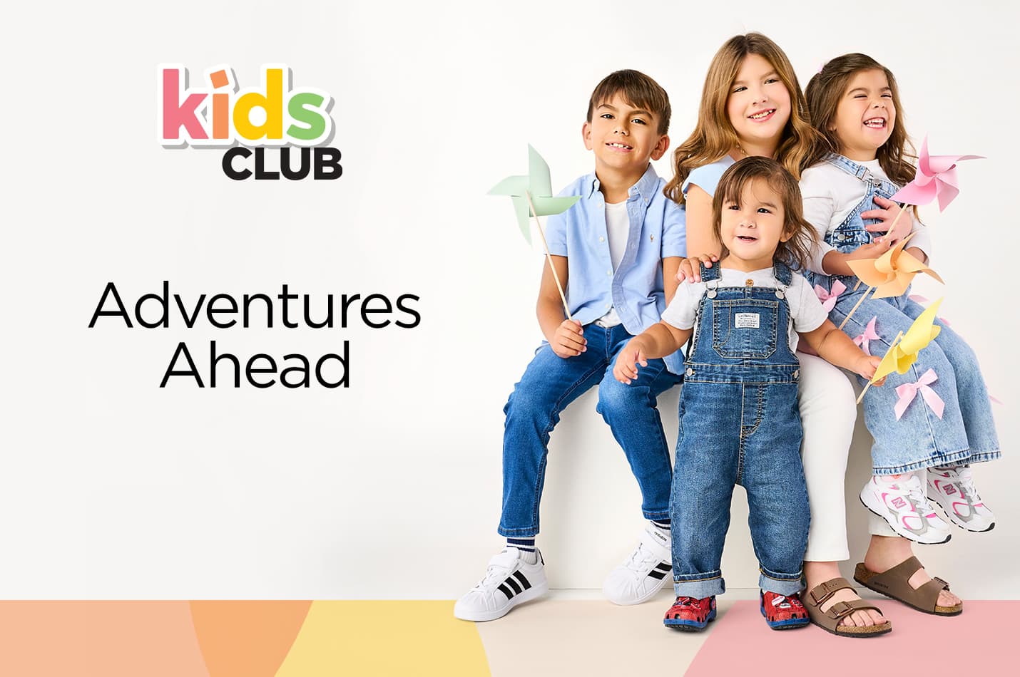 Three siblings sitting on a white cube holding colorful pinwheels while wearing stylish and comfortable shoes and sandals.