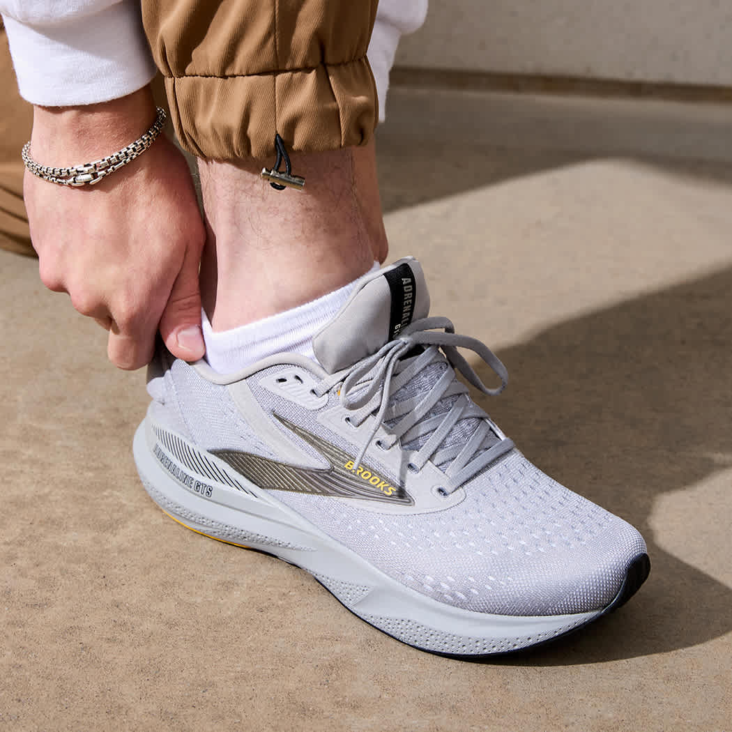 Close up lifestyle shot of someone slipping into a grey Brooks Adrenaline GTS 24 running shoes.